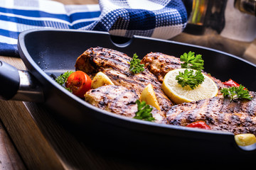 Grilled chicken breast in different variations with cherry tomatoes, green French beans, garlic, herbs, cut lemon on a wooden board or teflon pan. Traditional cuisine. Grill kitchen. 