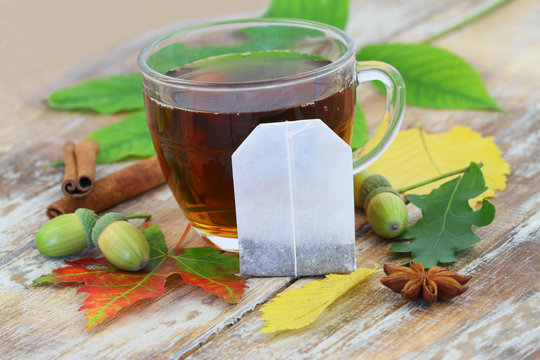 Tea bag leaning against glass with black tea, and autumn leaves
