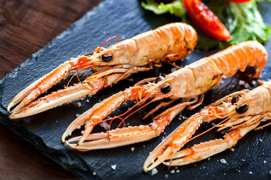 Macro close up of fresh grilled crawfish platter with green salad served on elegant black tile.