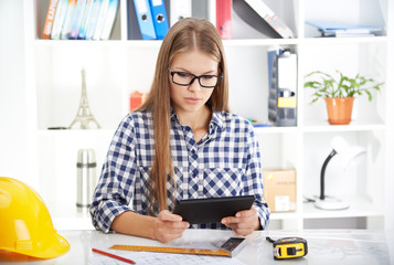Concentrated female architect with digital tablet studying construction plans. Young woman designer...