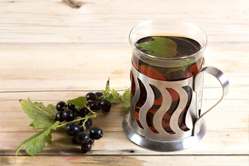 Black tea with black currant leaves in a glass and some black cu