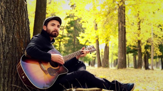 man playing an acoustic guitar in the woods