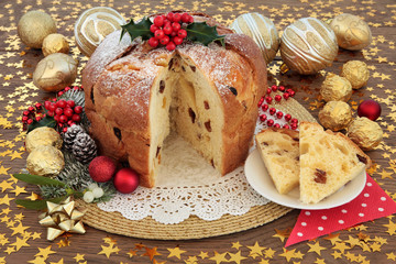 Panettone Cake. Panettone christmas cake and slice with bauble decorations, holly and winter flora over oak background with stars.