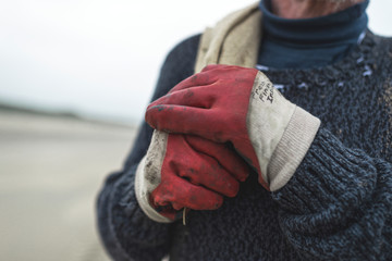 Close-up of work gloves from beachcomber holding burlap sack.