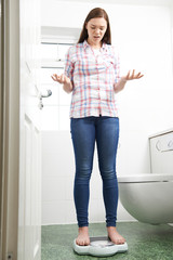 Unhappy Teenage Girl Standing On Bathroom Scales