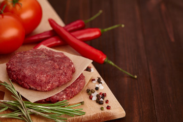 Raw meat for burgers with spices on wooden board