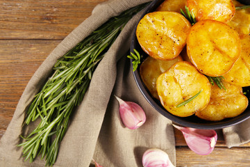 Delicious baked potato with rosemary in bowl on table close up