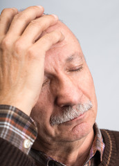 Obraz premium Elderly man suffering from a headache on a gray background
