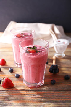 Glasses of berry smoothie on wooden table on dark background