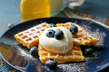 Sweet homemade waffles with blueberries and cream on plate, on dark wooden background