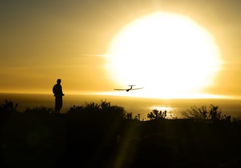 person flying toy plane over ocean with sun setting in the background