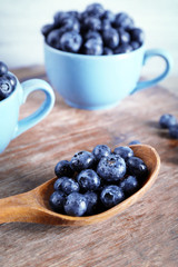 Fresh blueberries in cup and spoon on wooden table close up