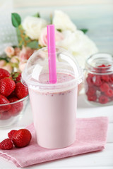 Plastic cup of milkshake on light wooden background