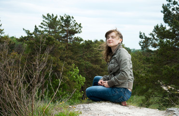 Young girl sitting on a hill in the forest. Meditation