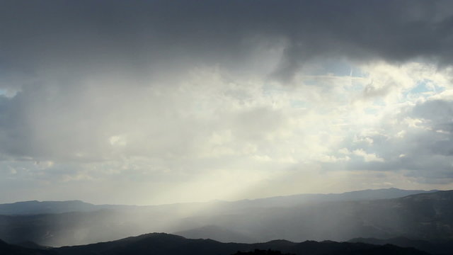 Beautiful rainy dawn in mountains, sunlight rays shining through cloudy sky