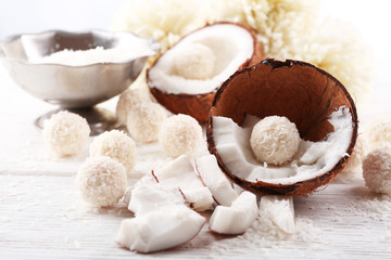 Candies in coconut flakes and fresh coconut on  light wooden background