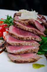 Medium rare steak served on a plate with cherry tomatoes and arugula. On top of it is grated parmesan cheese.