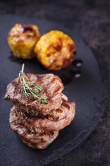 Pieces of red meat, steaks with vegetable and spices, served on black stone surface. selective focus