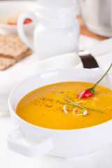 Vegetable soup with pumpkin, carrot, red pepper and cream in white bowl on white background.