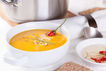 Vegetable soup with pumpkin, carrot, red pepper and cream in white bowl on white background.