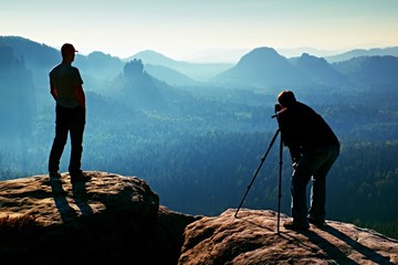 Tourist guide and photo enthusiast stay with tripod on cliff and thinking. Dreamy fogy landscape,...