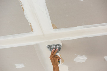 man hand with trowel plastering a ceiling, skim coating plaster