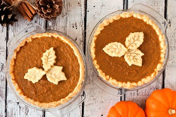 Two autumn pumpkin pies with leaf pastry toppings against rustic wood background © Jenifoto