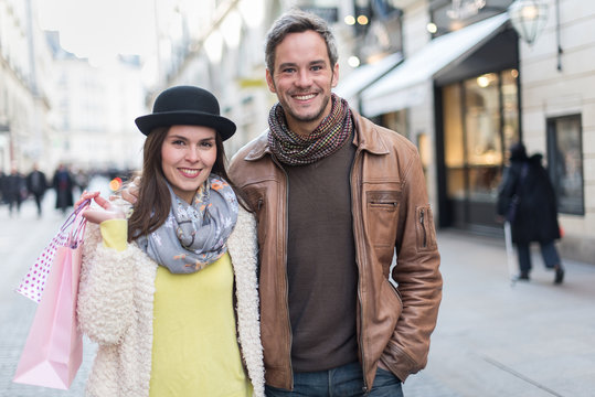 A trendy couple is walking arm in arm in the city center