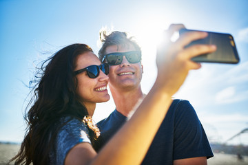 smiling couple taking selfies with smartphone on the sunny beach