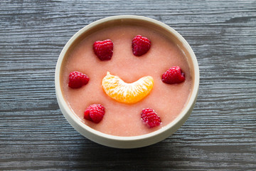 Cup of pink guava juice with raspberries and orange smile over dark wooden background
