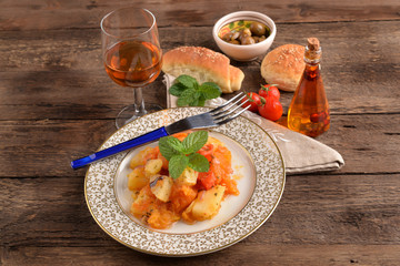 Golden dish of pumpkin and potatoes with wine goblet on wooden table