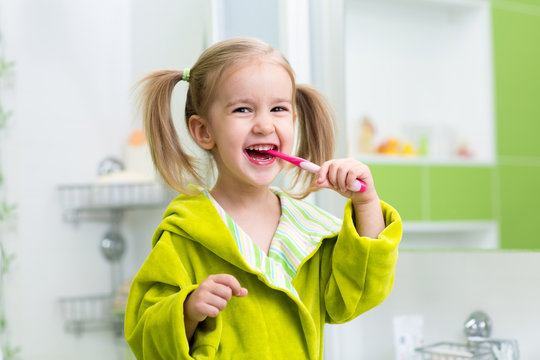 Smiling little girl brushing teeth in bathroom