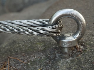 Detail of steel bolt anchor eye in rock. The end knot  of steel rope. Climbers path in rocks via ferrata. Iron twisted rope fixed in block.