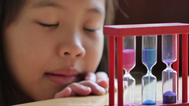 Little Asian child looking at hourglass in class