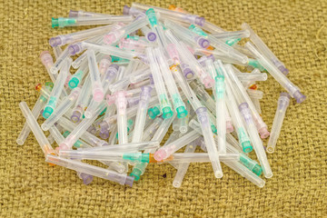 Many used disposable needle lie strewn on brown sack fabric