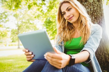 Fototapeta premium Smiling woman using digital tablet while sitting under tree 