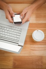 Man using mobile phone while laptop and disposable cup on desk