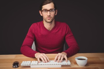 Serious man typing on keyboard with coffee on desk
