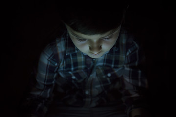 Niño iluminado por la luz de la pantalla de su tablet o e-book