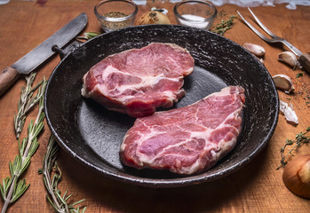 Juicy fresh raw pork steak old cast iron pans with a knife for meat fork herbs and spices and garlic on wooden rustic background close up
