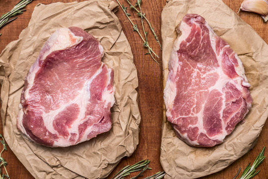 two Fresh raw pork steak on paper with herbs  on wooden rustic background close up top view