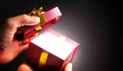Hands opening a red gift box with ribbon in shadow