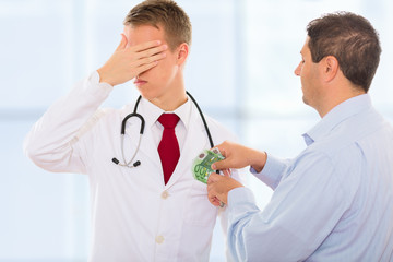 Man putting bribe money into a corrupt doctors coat while he is covering his eyes