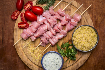 raw slices of turkey on skewers couscous herbs cherry tomatoes and garlic sauce on round cutting board  on wooden rustic background close up top view