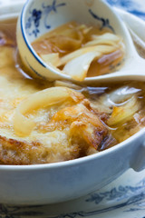 Französische Zwiebelsuppe mit Käse überbacken in Suppenschale mit Porzellan-Suppenlöffel auf französischem Geschirr in Nahaufnahme