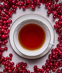 Plakaty  biała filiżanka herbaty na spodku na białym drewnianym tle ramka z czerwonych jagód Kalina z bliska widok z góry