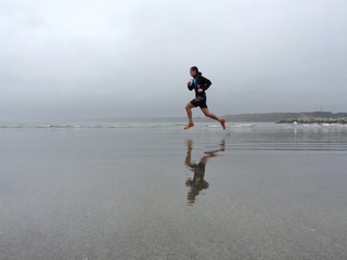 Beach runner and his reflection in the sea water