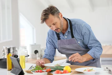 Crédence de cuisine en verre imprimé Cuisinier Man in kitchen cooking dish and using digital tablet