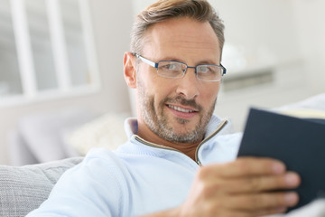 40-year-old man relaxing in sofa reading book