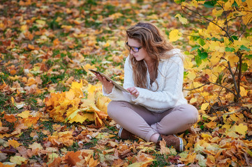 beautiful young woman with a tablet sitting in the autumn park